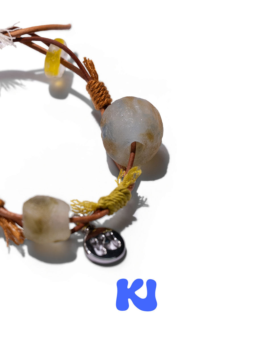 Rope bracelet detail with gray beads, yellow wrapping, and clear charm element