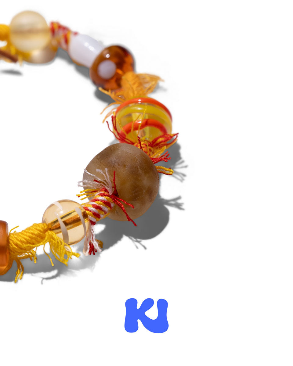 Close-up of round brown bead and glass beads on braided cord with orange fringe.